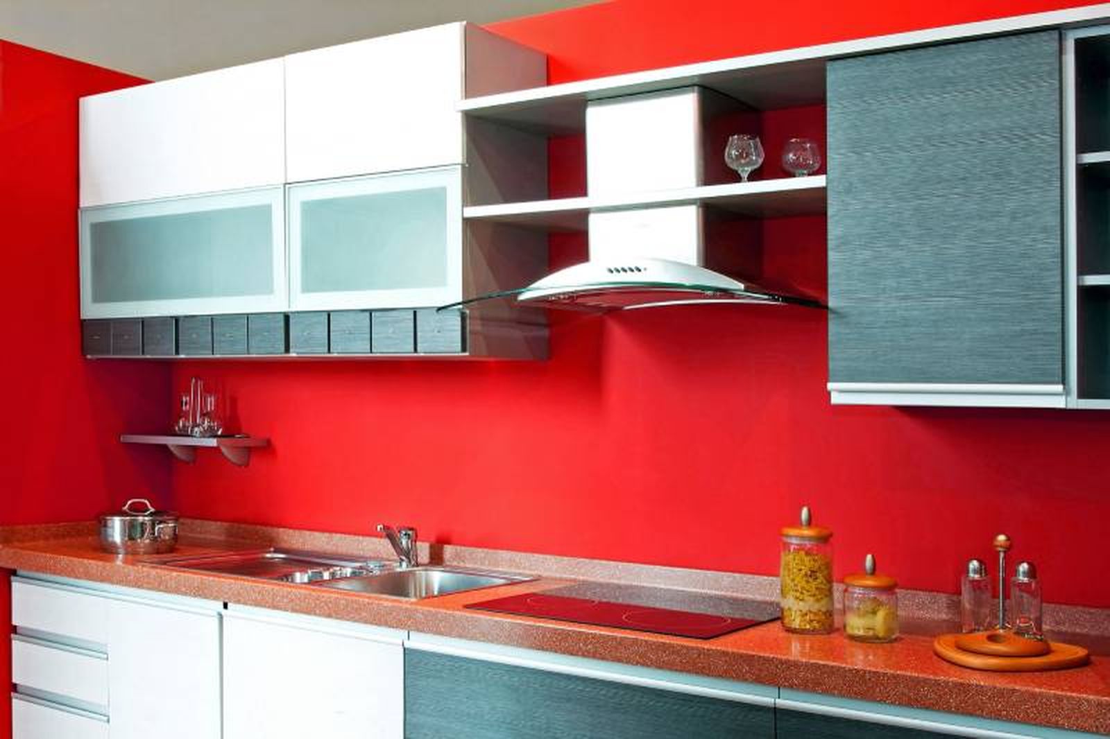 Cocina con pared en color rojo y muebles en blanco, gris y plateado.
