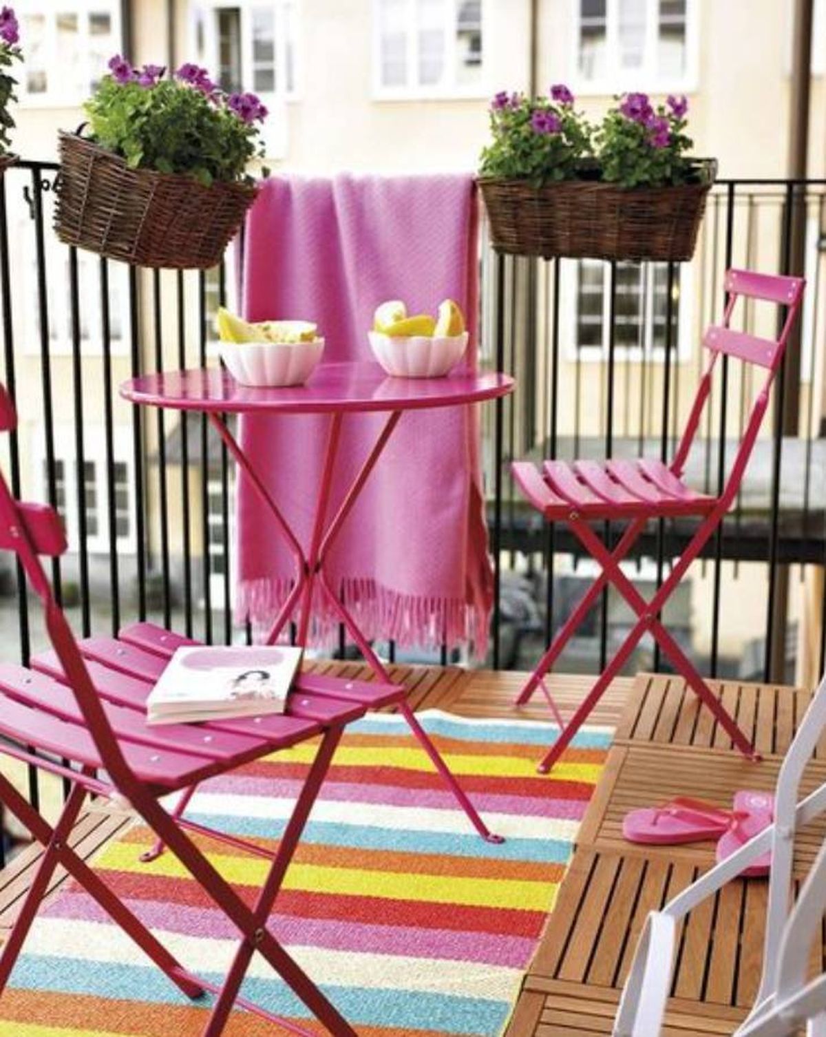 Balcón pequeño decorado con mesa y sillas rosas.