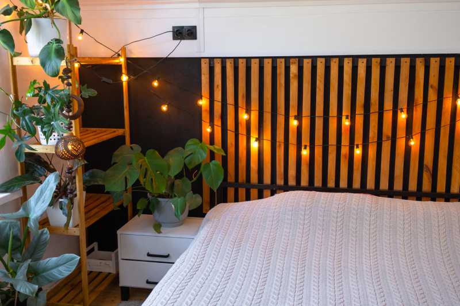 Dormitorio decorado con plantas y cabecero con guirnalda de luces.