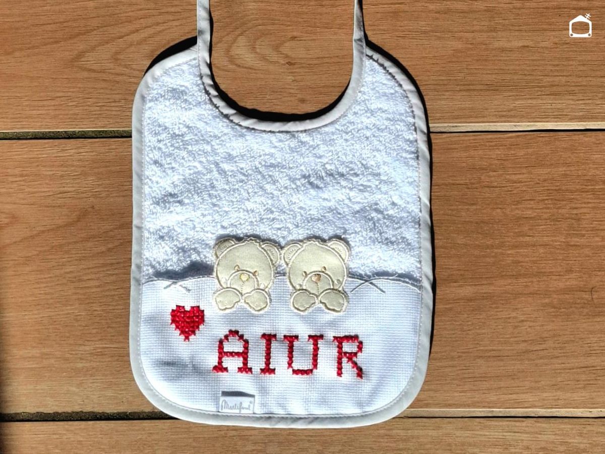 Babero con el nombre Aiur bordado en punto de cruz.