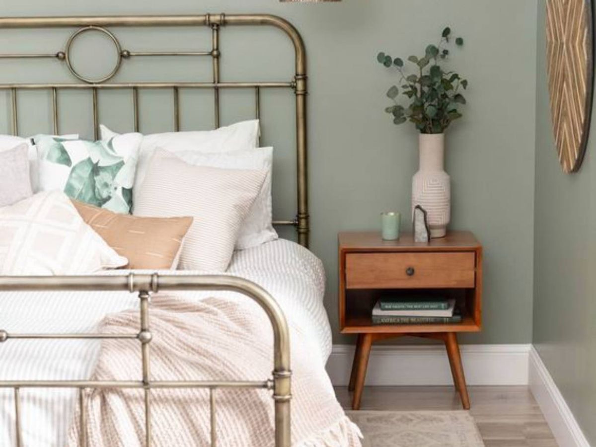 Un cabecero de forja dorada aporta elegancia a este dormitorio con pared verde.