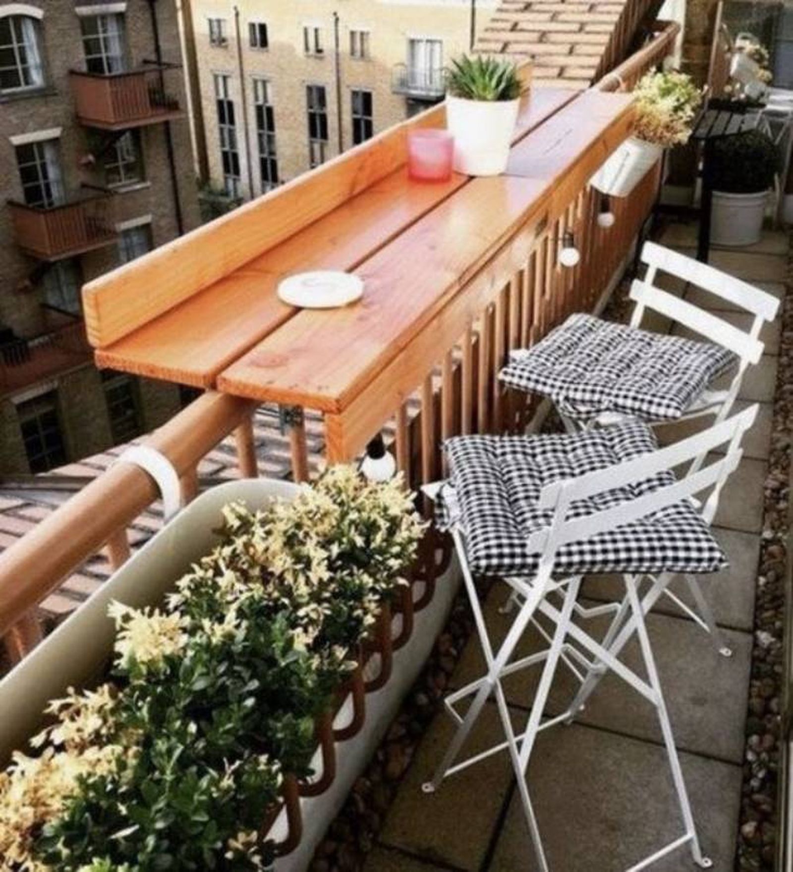 Balcón pequeño con sillas de metal blancas y mesa de barandilla de madera.