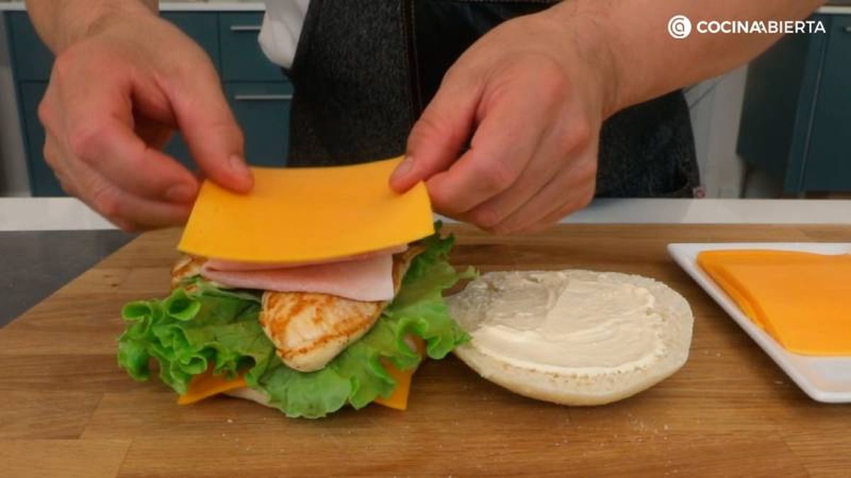 Rellena el bocadillo con tomate, lechuga, pollo, jamón york y queso cheddar