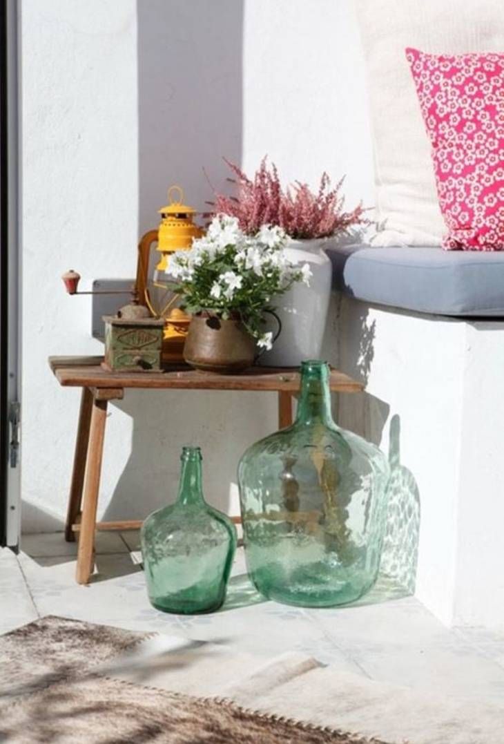Patio exterior decorado con dos damajuanas verdes de diferente tamaño.
