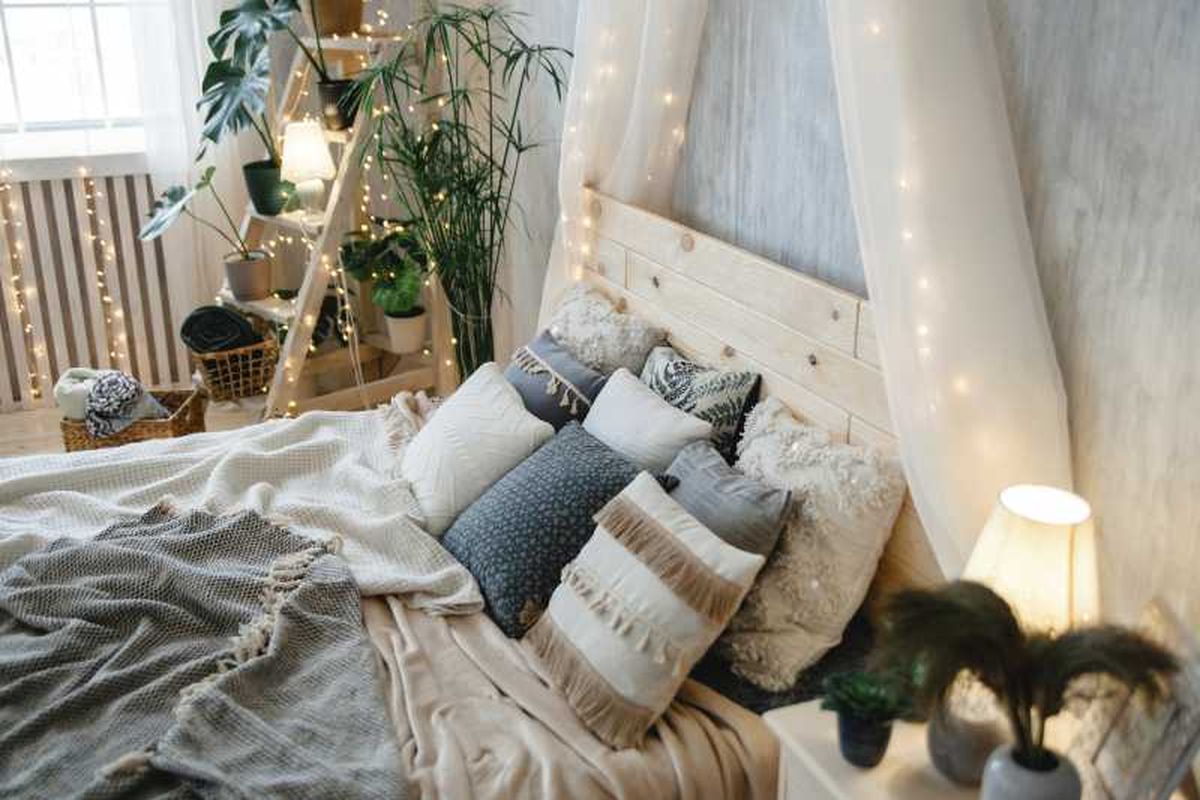 Dormitorio acogedor con mantas, luces y plantas.