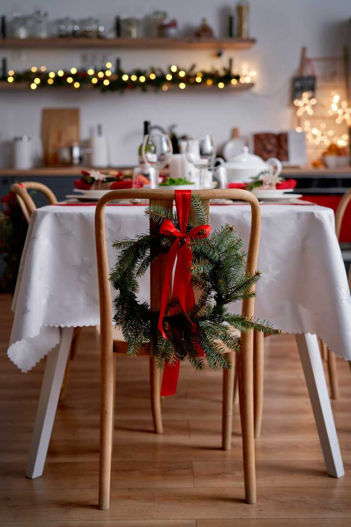 Mesa del comedor con las sillas decoradas con un lazo rojo y ramas de pino.