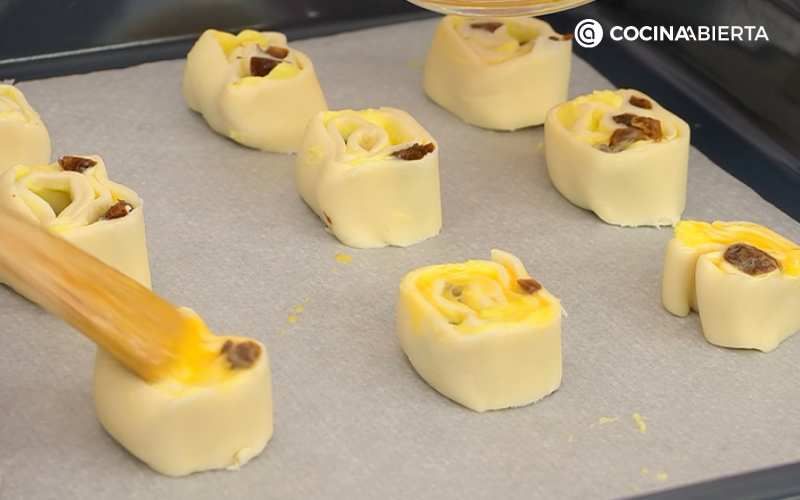 Pinta las caracolas de crema y pasas con huevo batido