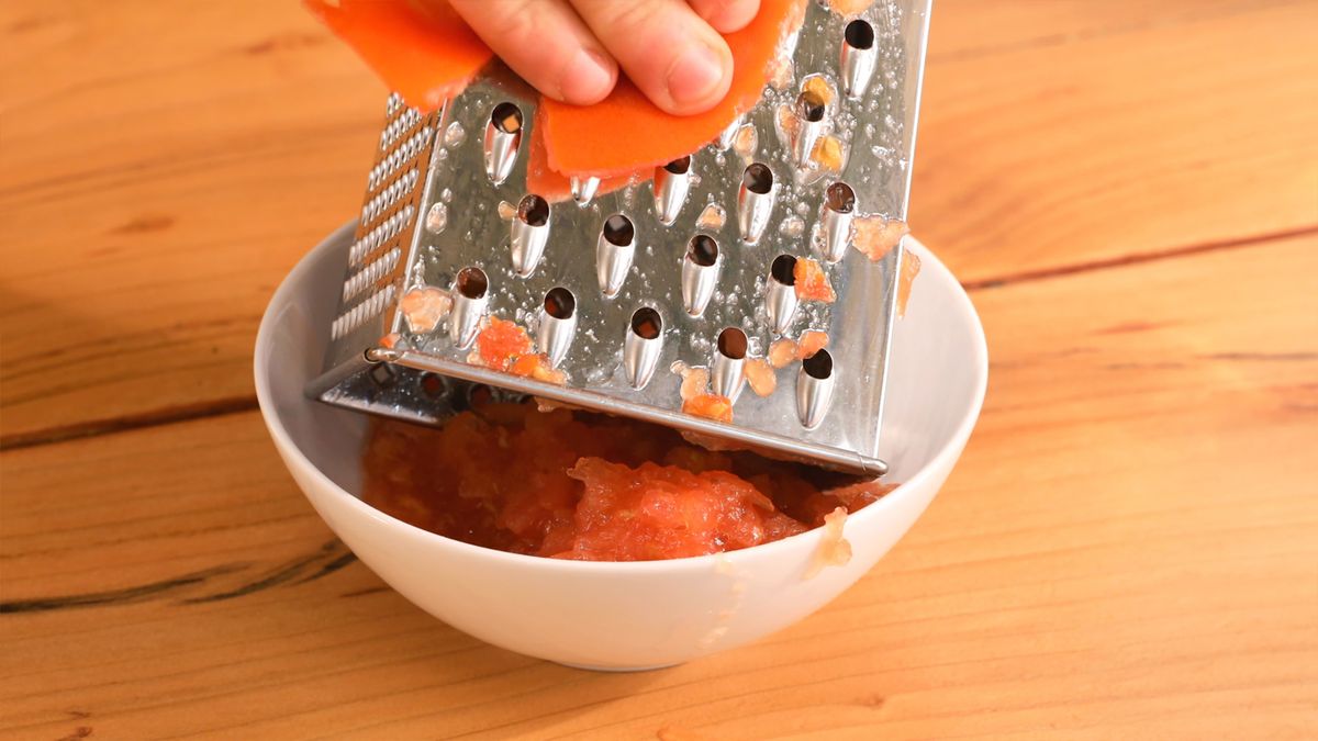 Lava y parte el tomate por la mitad, luego ralla la pulpa en un bol para incorporar su frescura