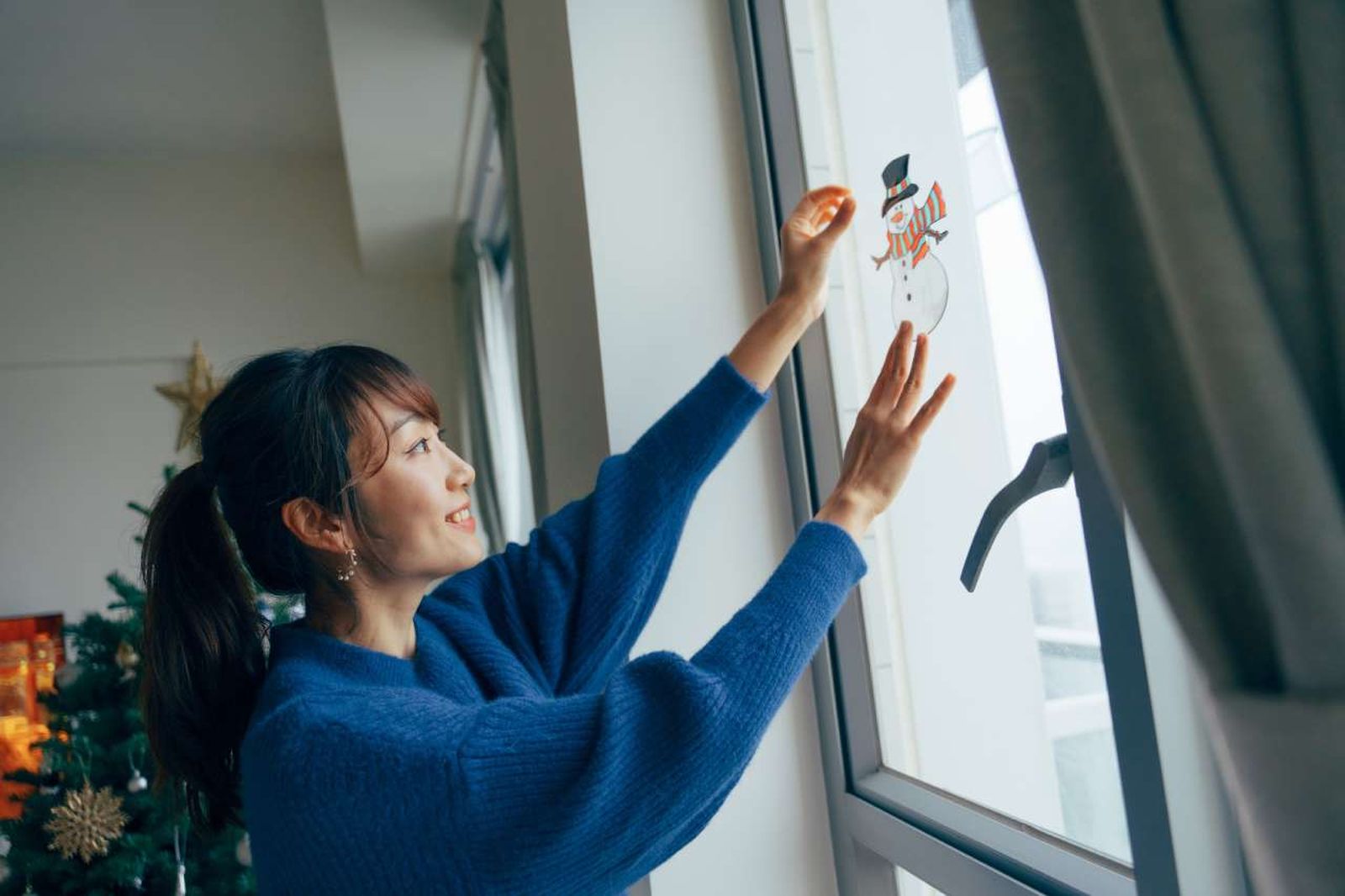 Mujer colocando un sticker adhesivo decorativo de Navidad en la ventana.