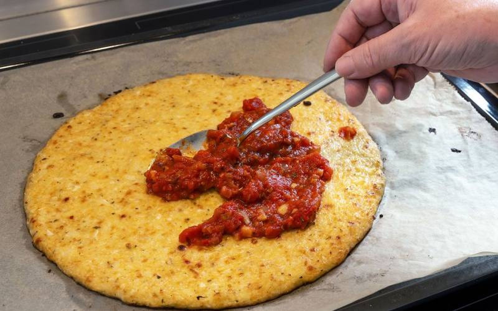 Extiende una capa de tomate por la masa de pizza de coliflor antes de poner más ingredientes