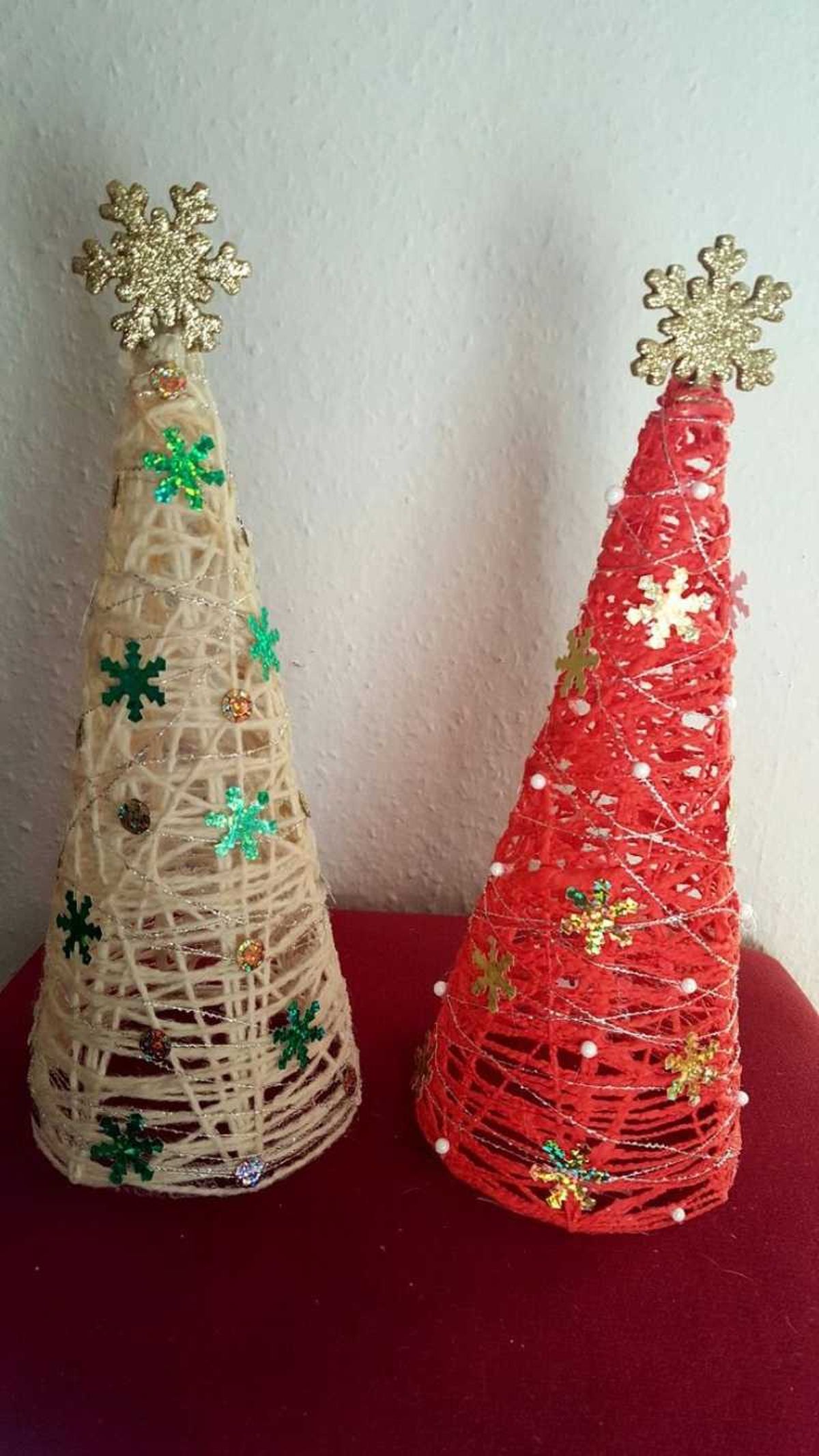 Árboles de Navidad hechos con hilo o lana con pequeñas decoraciones.