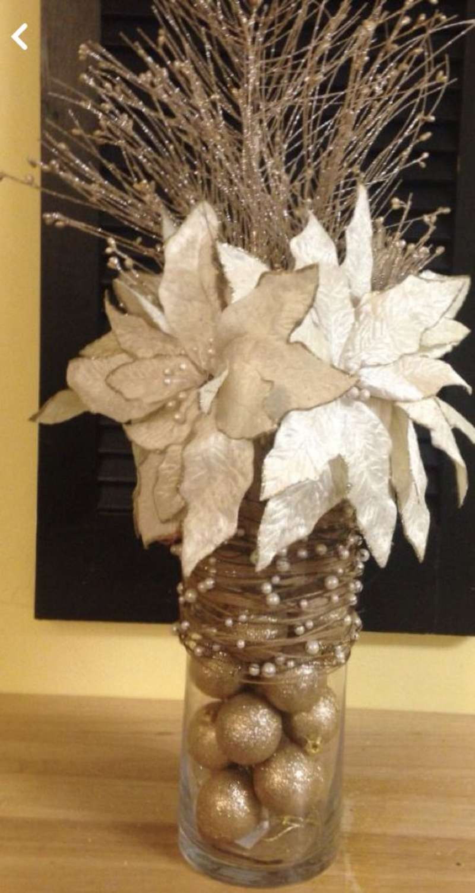 Jarrón de Navidad decorado con flores y adornos dorados.