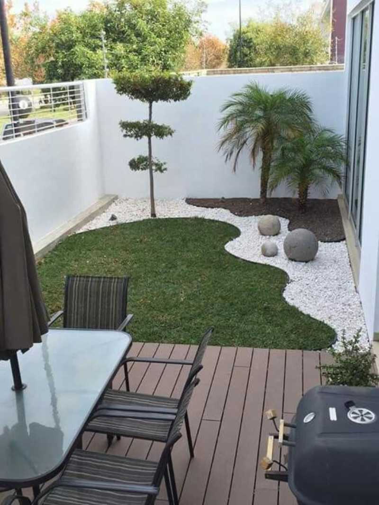 Jardín pequeño con césped artificial y piedras con barbacoa.