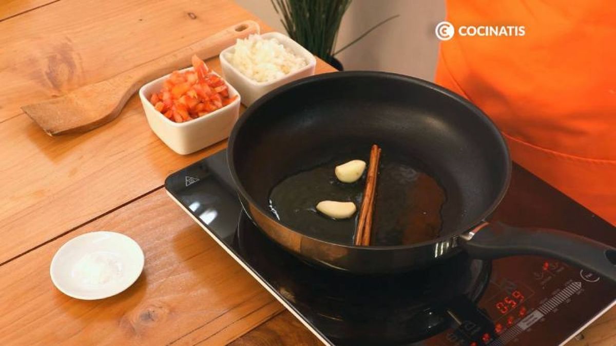 Pon la sartén al fuego y añade la rama de canela y el ajo