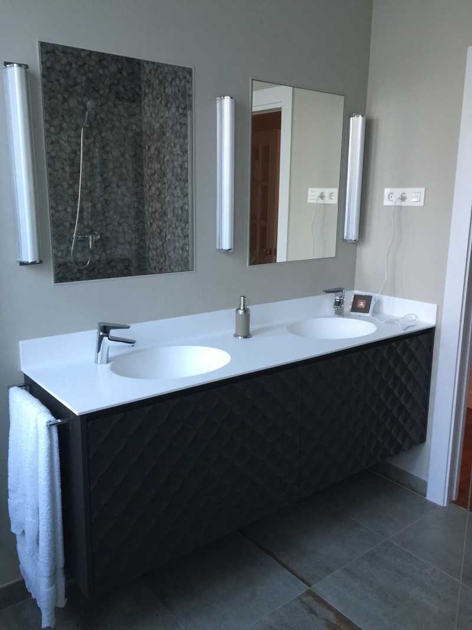 Baño principal con lavabo doble, dos espejos y apliques verticales.