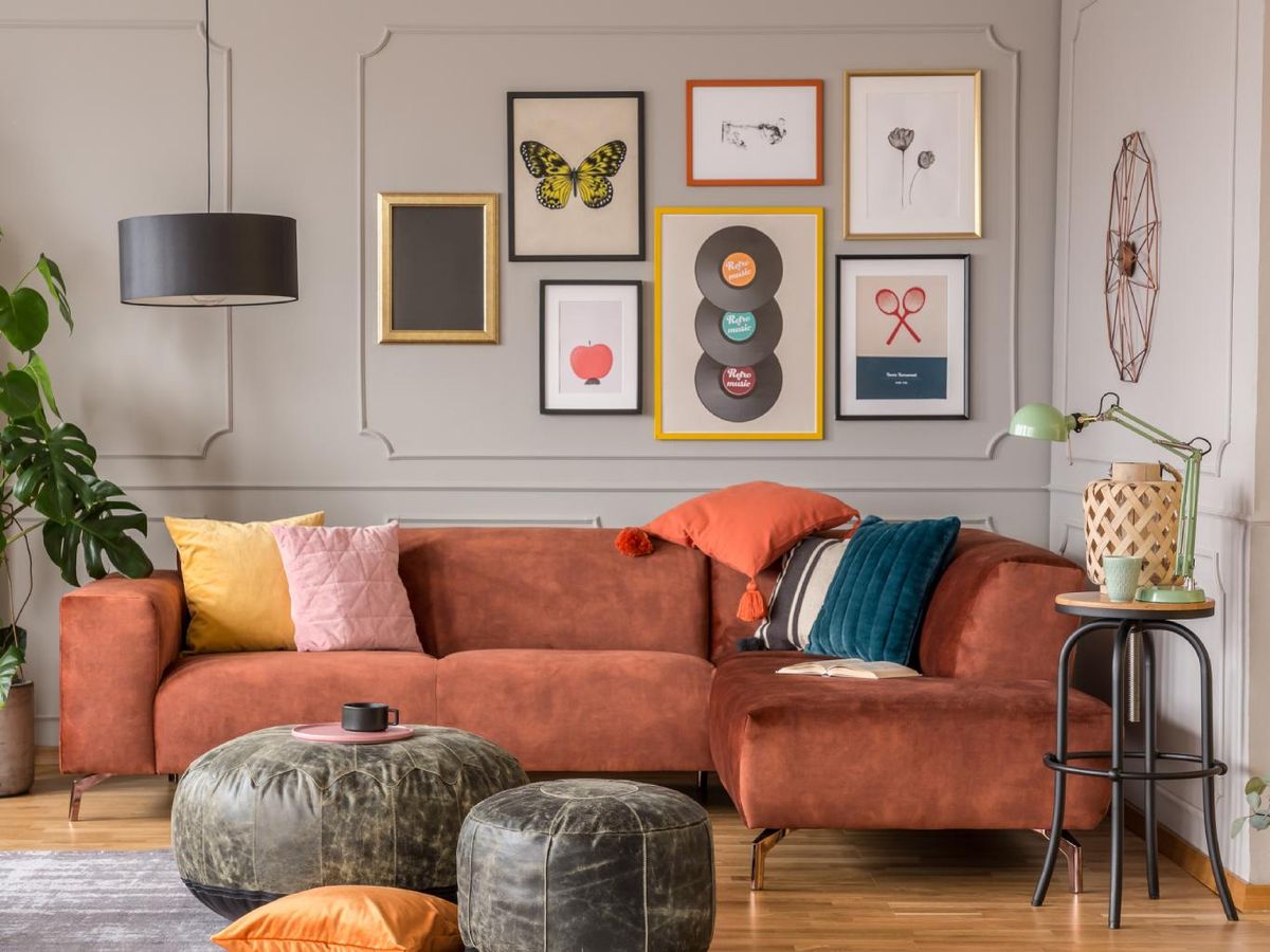 Salón ecléctico con sofá naranja y decoración en la pared.