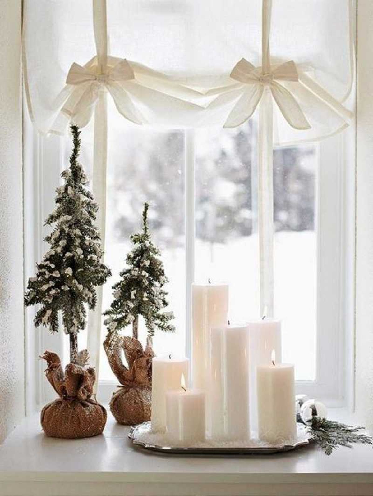 Ventana decorada con velas y mini árboles de Navidad.