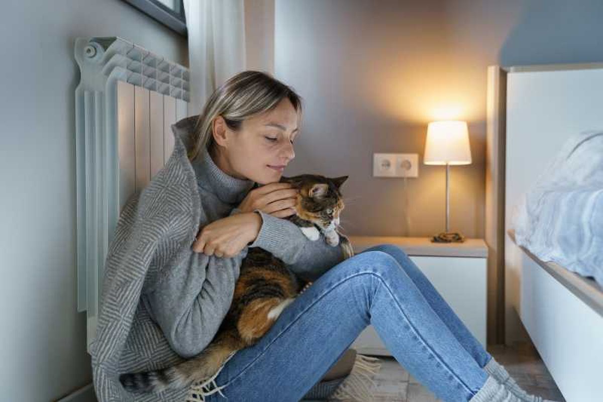 Mujer con un gatito frente a un radiador.