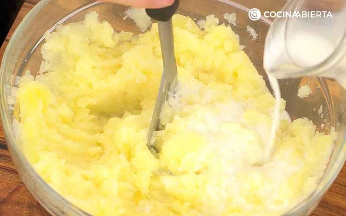 Agrega la leche mientras machacas las patatas