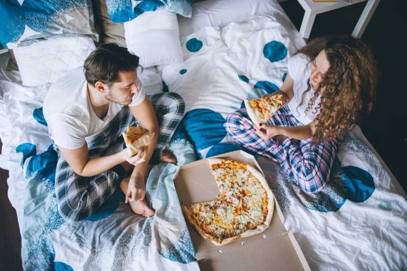 Hombre y mujer comiendo pizza en la cama.