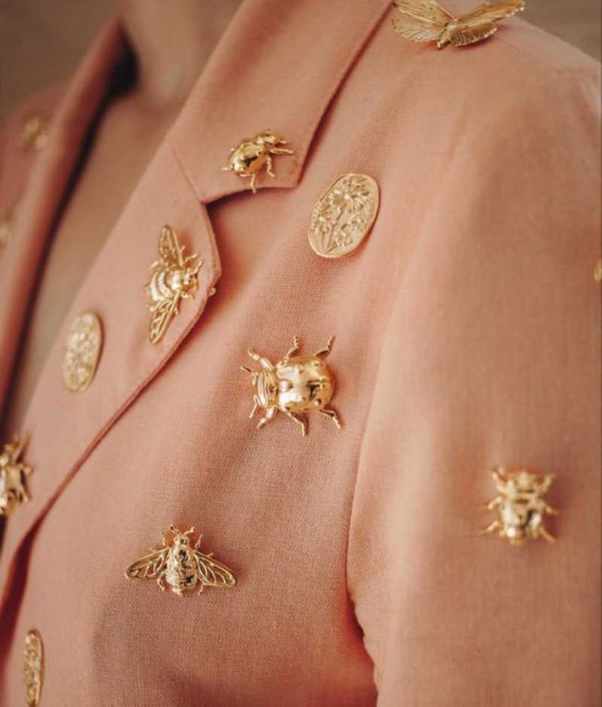 Blazer salmón con pines de escarabajos dorados.