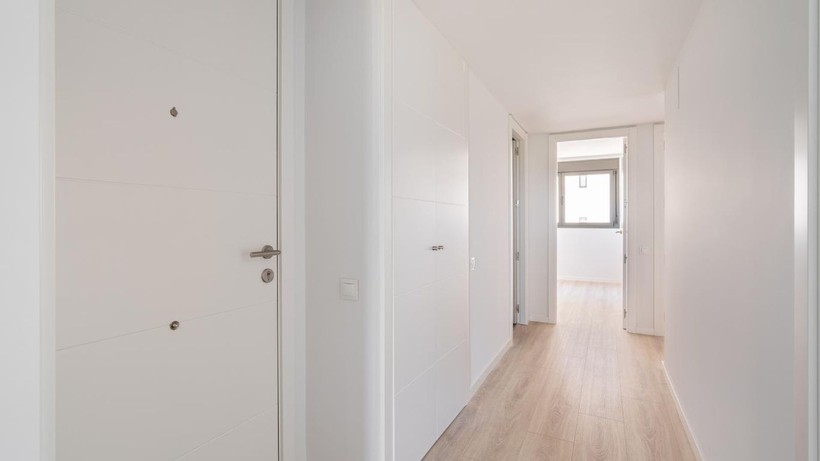 Pasillo largo y estrecho blanco y con madera clara.