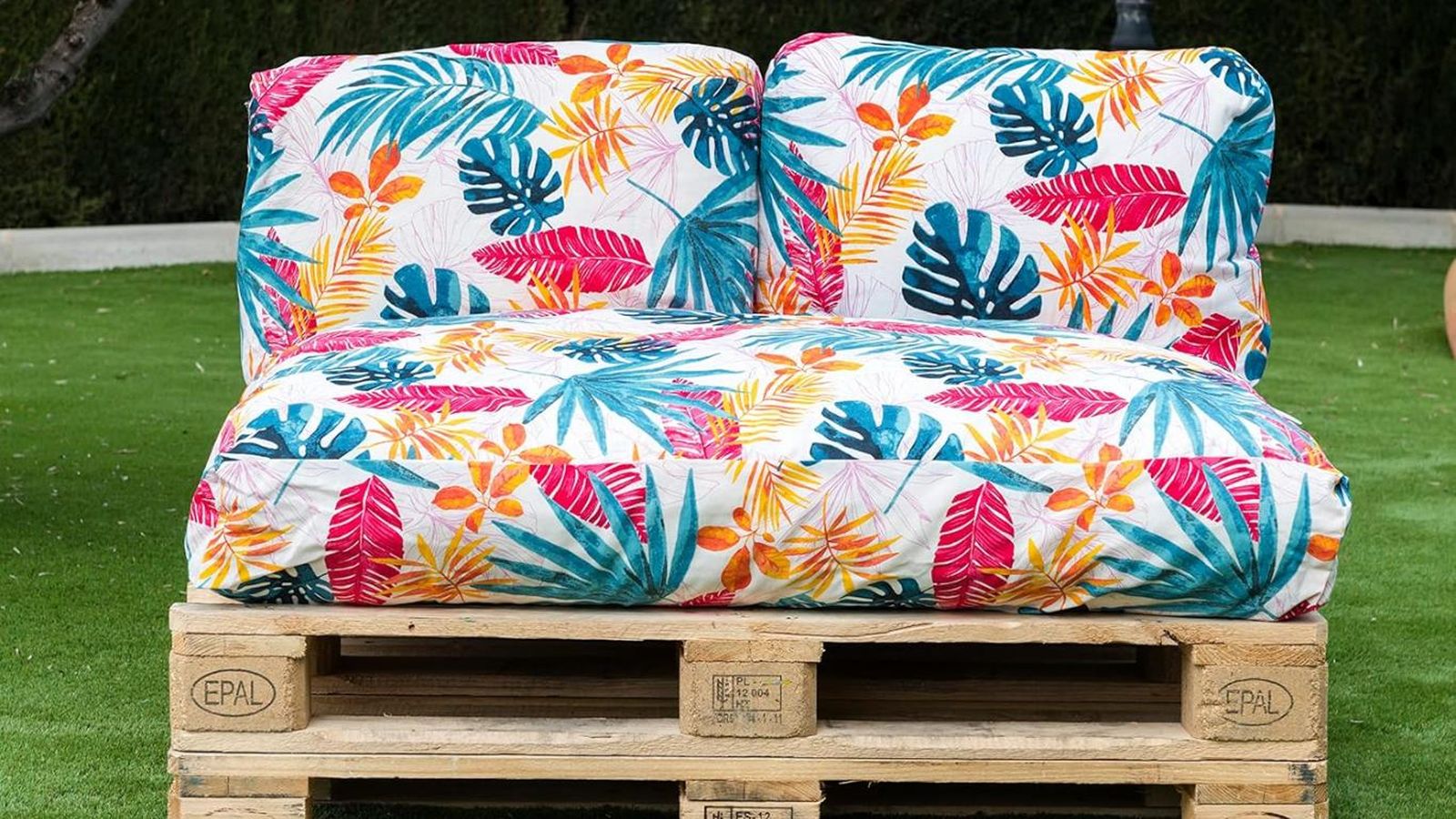 Sofá hecho con palets con cojines coloridos de estampado tropical.