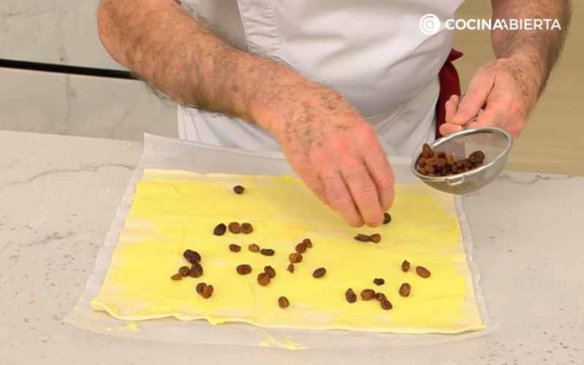 Cubre la lámina de hojaldre con crema pastelera y pasas
