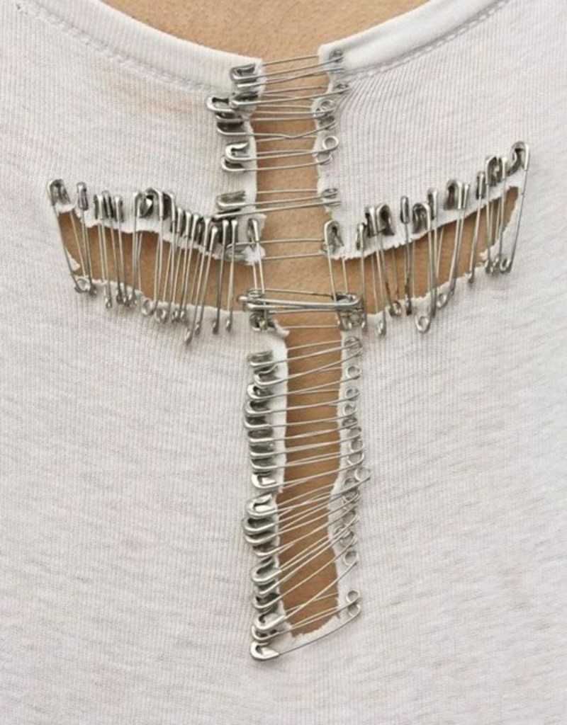 Camiseta cortada con una cruz hecha con imperdibles.