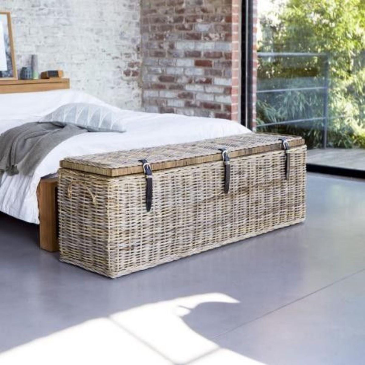 Dormitorio con baúl vintage de fibras naturales a los pies de la cama.