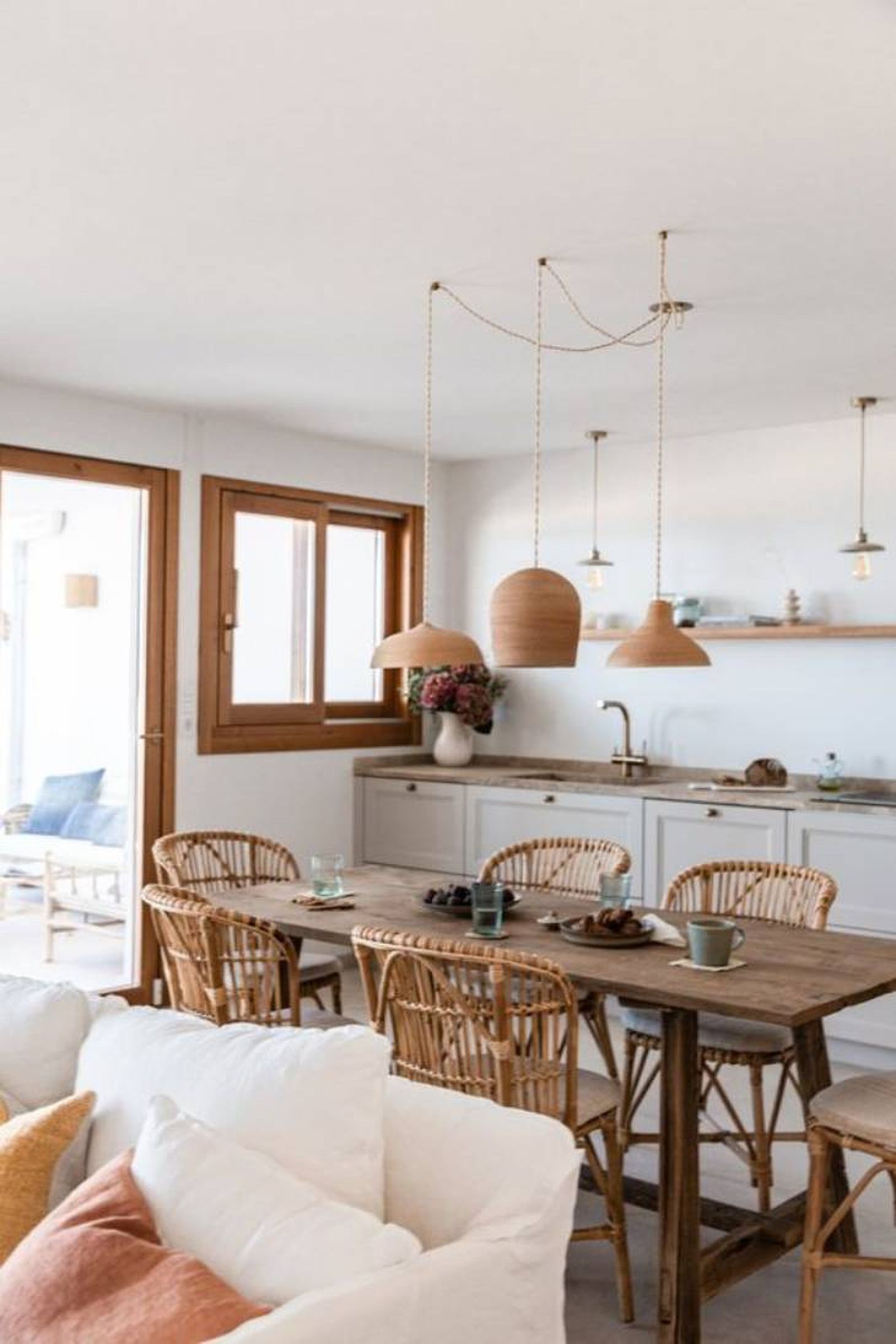 Cocina de estilo mediterráneo con mesa y sillas de madera y lámparas de fibras naturales.