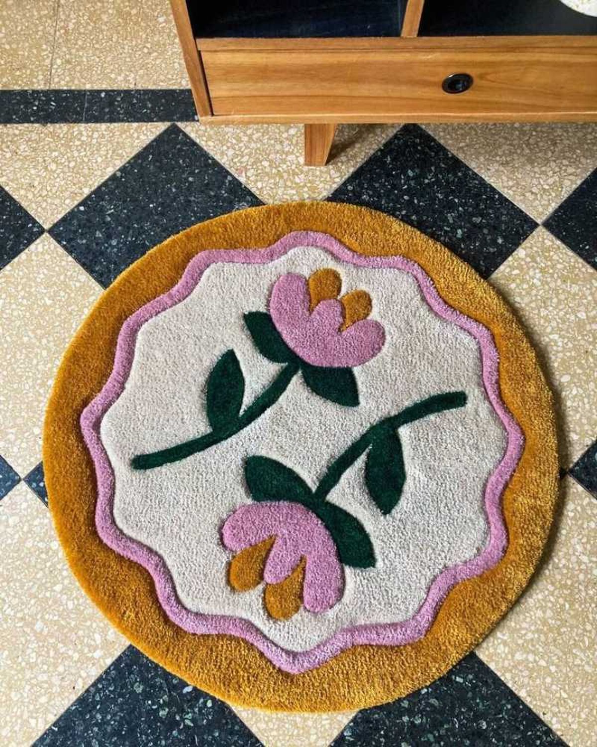 Alfombra artesanal redonda con flores rosas.