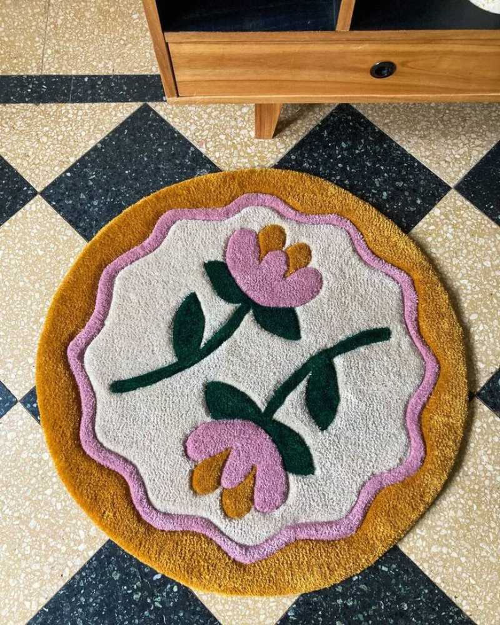 Alfombra artesanal redonda con flores rosas.