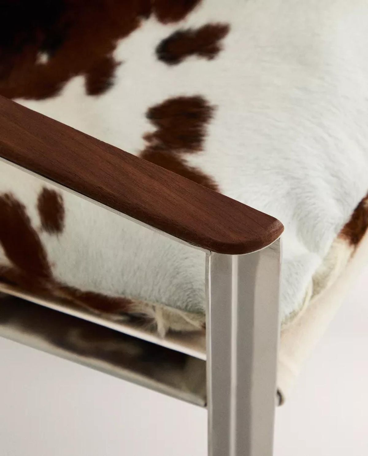 Butaca de piel bovina con estructura metálica y reposabrazos de madera.