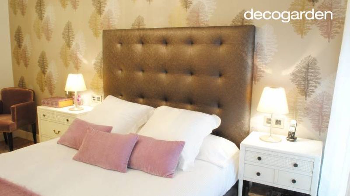 Dormitorio principal con cabecero acolchado y papel pintado de estampado vegetal.