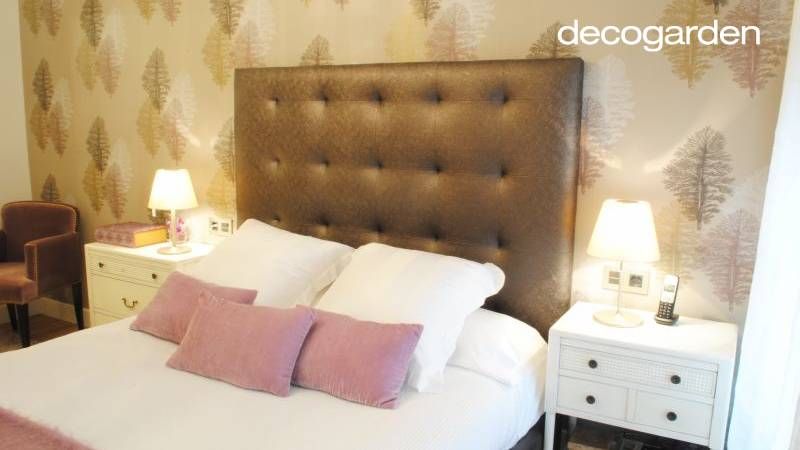 Dormitorio principal con cabecero acolchado y papel pintado de estampado vegetal.