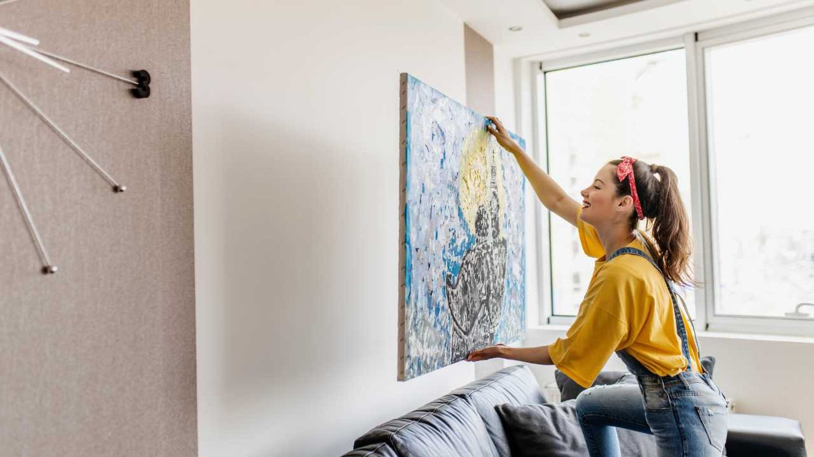 Mujer decorando la pared del salón con un cuadro.