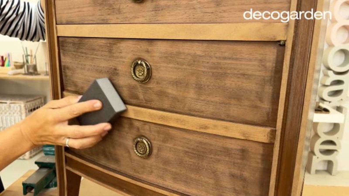 Mano lijando un mueble antiguo de madera con una esponja de tiza.