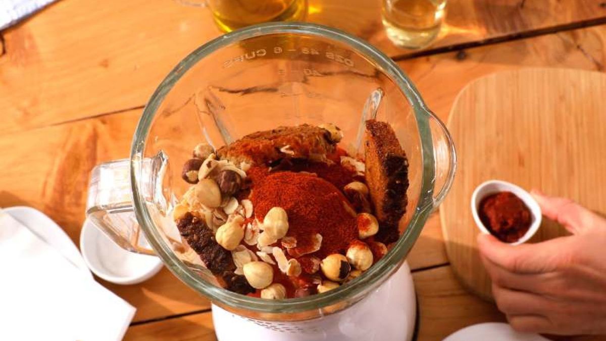 Combina ajo asado, tomate, pan, frutos secos y especias en la batidora para crear una salsa romesco rica y sabrosa