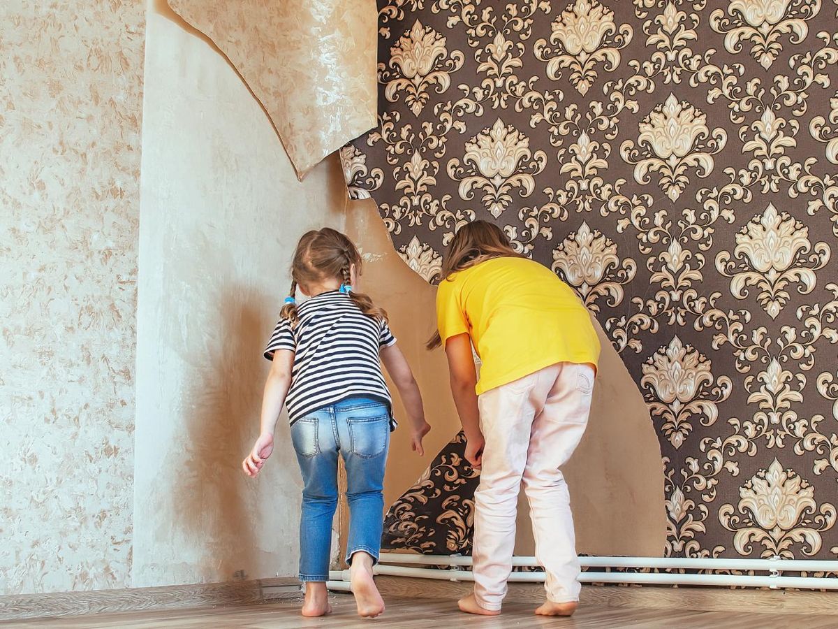Niñas despegando papel pintado anticuado.
