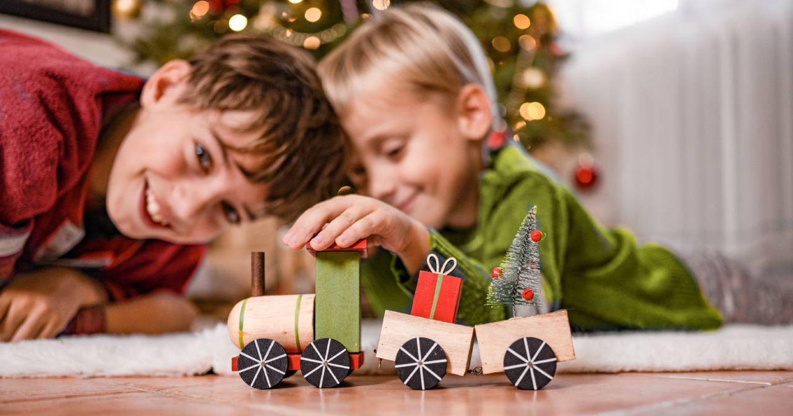 Niños jugando con un tren de madera en un rincón navideño.