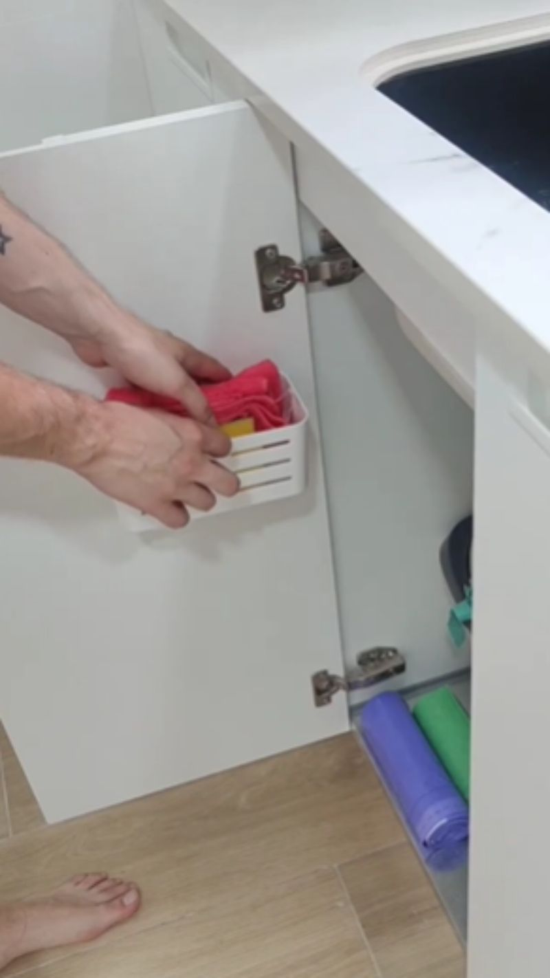 Cesto para estropajos detrás de la puerta del armario del fregadero.