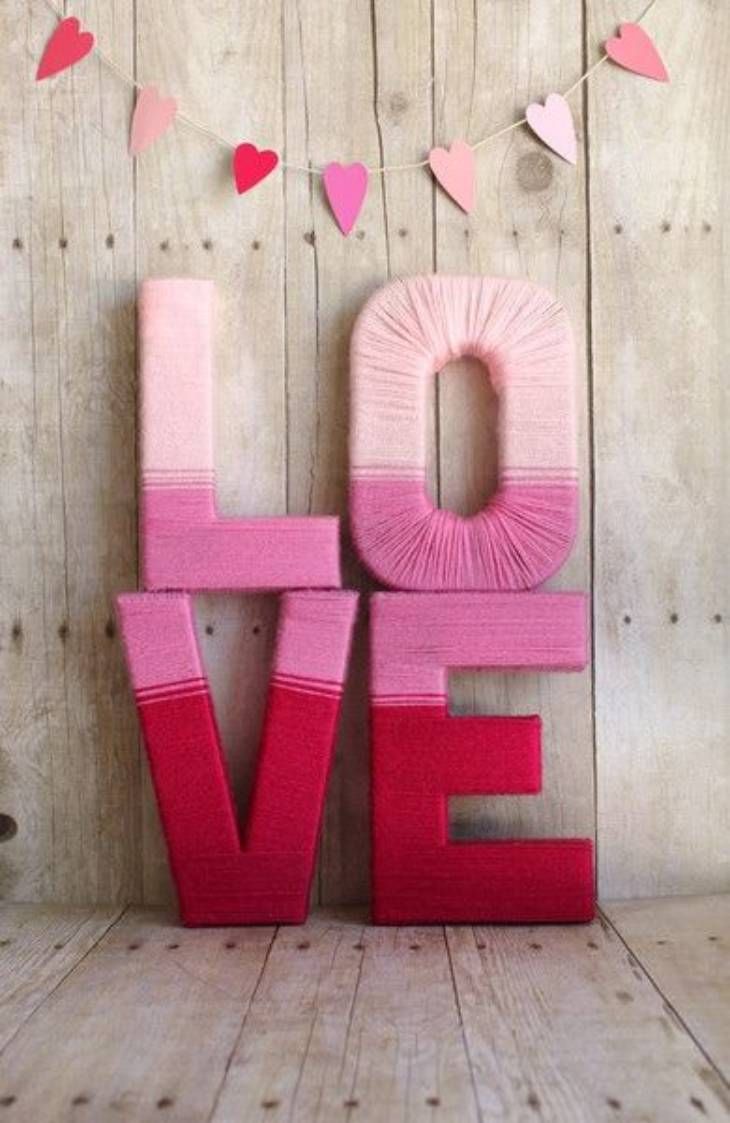 Letras LOVE decoradas con lana en tonos rosas y rojos.